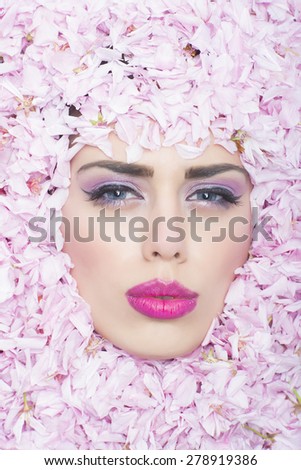 Pretty face of woman with bright make up in frame of pink flowers of japanese cherry blossom looking forward on colorful natural background, vertical picture