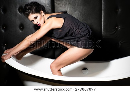 Woman sitting on bathtub  wearing black tank top in dark bathroom