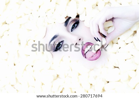 Portrait of fashionable young beautiful girl face in corn sticks heap looking forward on light food background copy space, horizontal picture