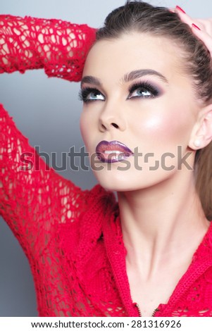 Portrait of pretty young girl in red knitted jacket with bright make up and beautiful neck looking away standing on grey wall background, vertical picture