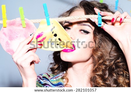 Portrait of sexy bright girl biting slice of cheese with pink lipstick kiss and bacon hanging on rope looking forward standing on grey wall background, horizontal picture
