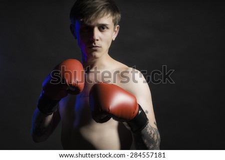 Young sexy muscular man in red boxing gloves standing in shadow looking forward on black background copy space, horizontal photo