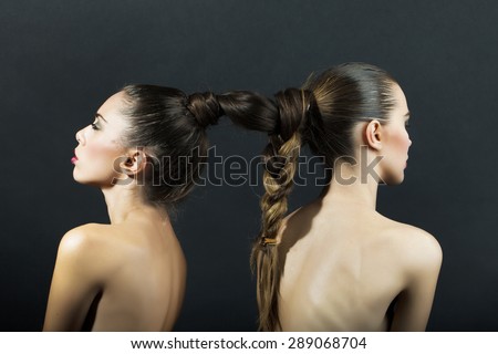 Pair of naked sensual attractive young girls standing back to back with beautiful brown woven hairdo on black background, horizontal picture