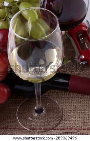 Two glass bocals with red and white wine with bottle and grapes on table closeup, vertical picture
