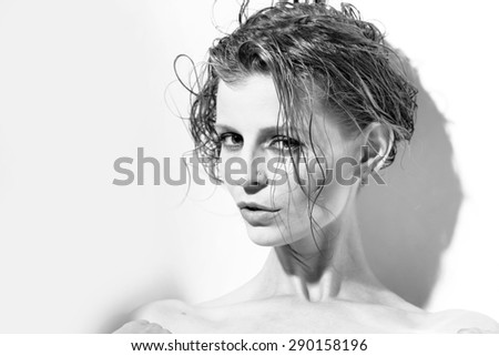 Portrait of sensual cool beautiful slim woman with wet short hair looking forward standing on studio wall background black and white, horizontal picture