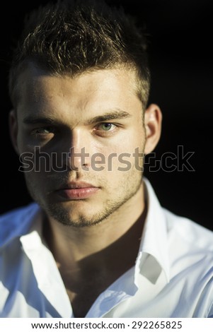 Portrait of young passionate handsome man model with beautiful face with dimple in white shirt in sunset on outdoor background, vertical picture