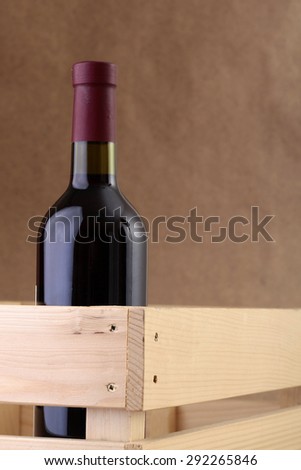 One glass bottle of red wine standing in wooden delivery box on burlap background copyspace, vertical picture