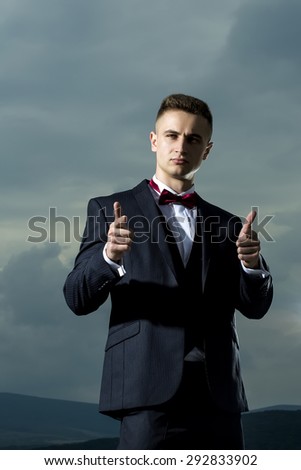 Handsome successful man in formal suit with bow tie standing on blue sky background, vertical picture