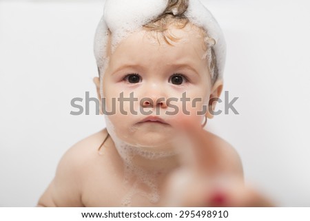Cute serious little boy one year with foam on his head in the bathroom looks forward, horizontal photo