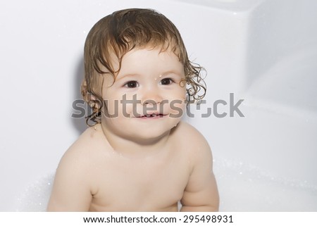 Closeup portrait of smiling curly wet baby boy with water droplets on face in white tub, horizontal photo