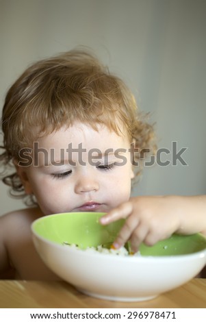 Portrait of small male kid with blonde curly hair and round cheecks eating from green plate with hand closeup, vertical picture
