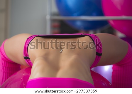 Closeup of beautiful sexual belly of fitness woman with musculat body lying in erotic pose on big pink ball in sport hall training indoor, horizontal picture