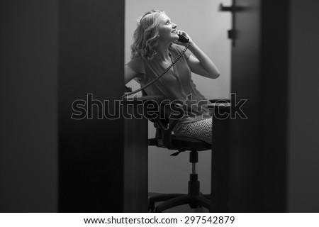 View from doorway of happy pretty secretary woman sitting in office with feet on table in blouse holding telephone receiver speaking on phone black and white, horizontal picture