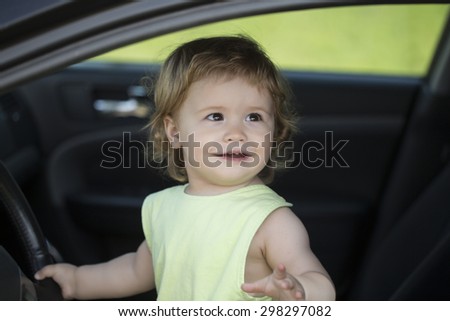 Pretty small funny male child driver sitting in big car with black salon holding wheel looking away through window in summer, horizontal picture