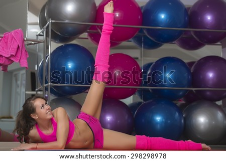 Sexy cute smiling sporty fitness girl in pink with flexible body stretching lying on floor in training hall on sport balls background copyspace, horizontal picture