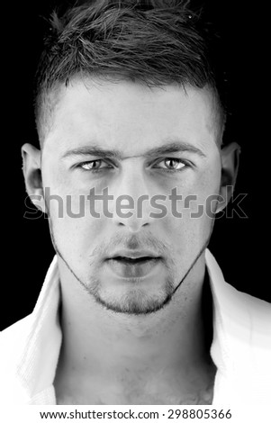 Portrait of sexy young handsome serious boy with unshaven face with scar and stylish hairdo looking forward standing in shirt with open collar black and white, vertical picture