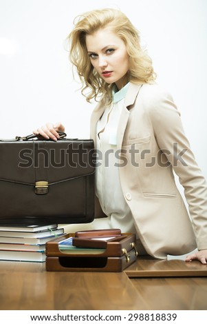 Sexual concentrated pretty young business woman with blonde curly hair near black leather briefcase looking forward standing on white background, vertical picture