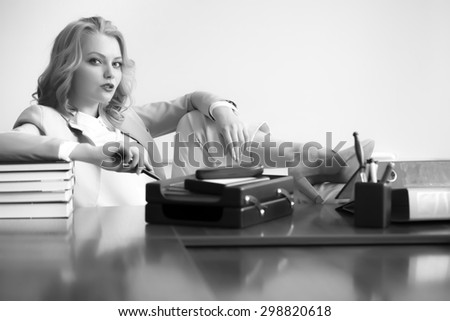 Beautiful sexy business woman boss sitting at table with many office appliances looking forward black and white copyspace, horizontal picture