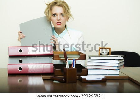 Pretty young blond business woman sitting in office at table with many documents files has a lot of work holding grey folder in hands on white background, horizontal picture
