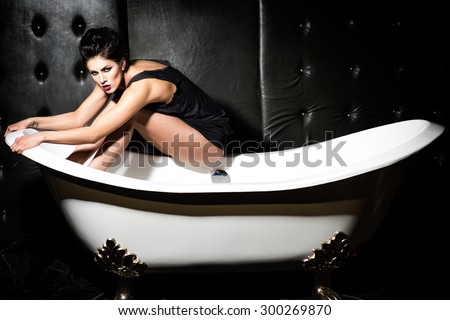 Woman sitting on bathtub  wearing black tank top in dark bathroom