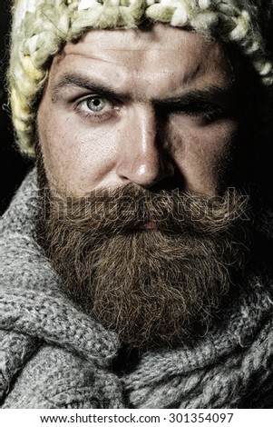 Portrait of unshaven homeless guy with long beard and hendlebar moustache in knitted yellow hat and grey scarf looking forward arching brow standing closeup, vertical picture