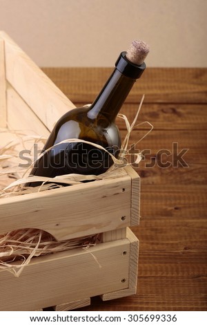 One glass wine corked new bottle full of alcohol red beverage wrapped in straw standing in wooden box on brown table top and paper background, vertical picture