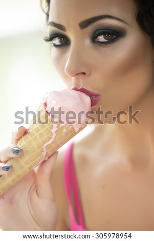 Closeup of sexual attractive young lady with bright makeup eating cold dessert of red berry ice cream cone with mouth looking forward, vertical picture