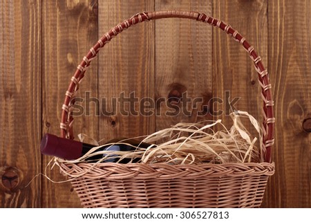 One glass wine corked new bottle full of alcohol red beverage wrapped in straw lying in wattled basket on wooden background, horizontal picture