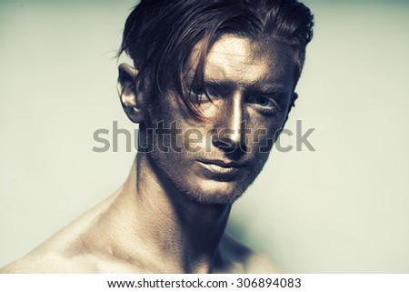 Portrait of young fashionable painted man model with bronze bodyart on face and stylish hairdo looking forward standing in studio on white background, horizontal picture
