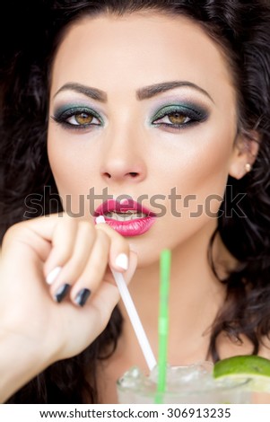Closeup of sexy pretty brunette woman with curly hair and bright makeup with alcoholic mojito cocktail from mint soda light rum ice cubes and lime with straw, vertical picture