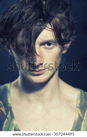 Portrait of handsome sexual stylish young unshaven boy model in undershirt standingwith modern hairdo looking forward indoor on studio background closeup, vertical picture
