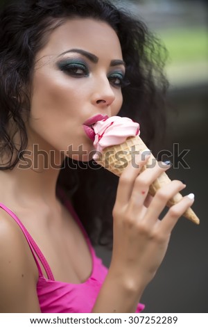 Portrait of sexual attractive brunette lady with curly hair and bright makeup eating cold dessert of red berry ice cream cone with mouth, vertical picture