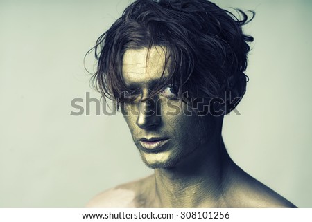 Portrait of young fashionable painted guy model with golden bodyart on face and stylish hairdo looking forward standing in studio on white background copyspace, horizontal picture