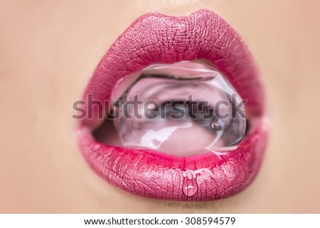 Closeup of sexy open female mouth of beautiful young woman with bright pink lips holding cold fresh crystal ice cube, horizontal picture