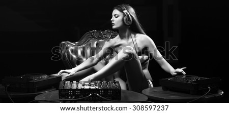 Pretty young glamour dj woman in lingerie and headphones sitting at table with mixer console on leather royal chair in night club on dark background black and white, horizontal picture