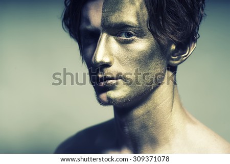 Portrait of young fashionable painted man model with golden bodyart on one half of face and stylish hairdo looking forward standing in studio on white background, horizontal picture