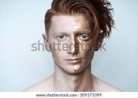 Portrait of young fashionable painted man model with bronze bodyart on one half of face and stylish red hairdo looking forward standing in studio on white background, horizontal picture
