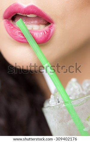 Closeup of sexual attractive brunette female open mouth of girl with pink lips drinking cold cocktail with many ice cubes and straw, vertical picture