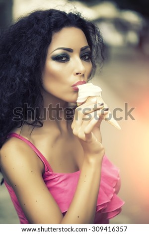 Sexual brunette pretty young lady with bright makeup eating cold dessert of red berry ice cream cone with mouth looking forward, vertical picture