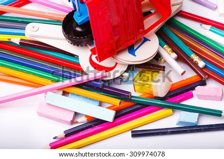 Colorful pencils of red yellow orange violet purple pink green blue chalk fan english alphabet and truck car toy lying on white school desk background, horizontal photo