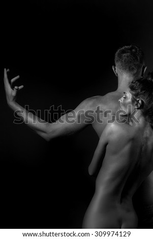 Pair of slim undressed woman embracing young man with sexual strong muscular attractive body with raised arms in sides and standing in studio black and white, vertical picture