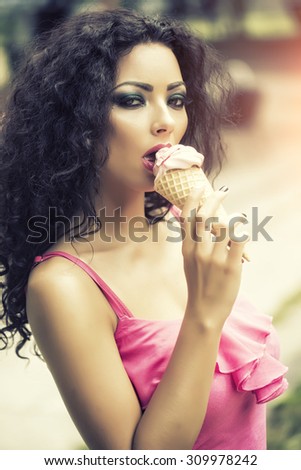 Portrait of sexual beautiful brunette lady with curly hair and bright makeup eating cold dessert of red berry ice cream cone with mouth, vertical picture