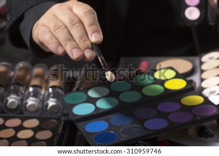 Colorful set of professional palette of eyeshadow green violet yellow purple black beige brown colors and male hand holding natural soft make-up brush, horizontal picture