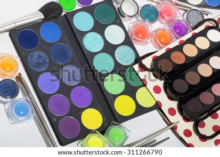 Set of different professional eyeshadow palette red orange green violet pink yellow purple black beige brown colors foundation powder and make-up brushes on white background, horizontal picture