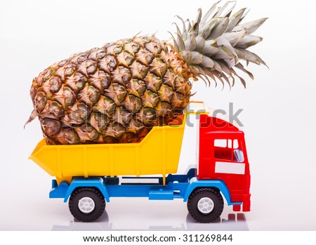 Plastic colorful toy truck yellow blue and red colors with one fresh big pineapple fruit in basket on white studio background closeup, horizontal picture