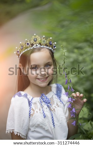 Portrait of beautiful smiling princess girl with long brunette hair in traditional ukrainian embroidery white blue colors and beautiful diadem with diamonds in gold outdoor, vertical picture