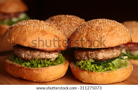 Few big delicious appetizing fresh burgers of green lettuce leaf cheese meat cutlet and white bread bun with sesame seeds on black background closeup, horizontal picture