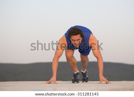 One muscular athlete runner sportsman with brunette hair in blue sportswear standing low on start ready for running looking forward outdoor on white background copyspace, horizontal picture