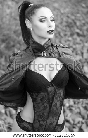 One sensual brunette young wild woman with bright make-up and ponytail in leather biker jacket and erotic lace lingerie looking away outdoor on natural background black and white, vertical picture