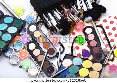 Set of many professional visagiste eyeshadow palette red orange green violet pink yellow purple black beige brown colors foundation powder and make-up brushes on white background, horizontal picture